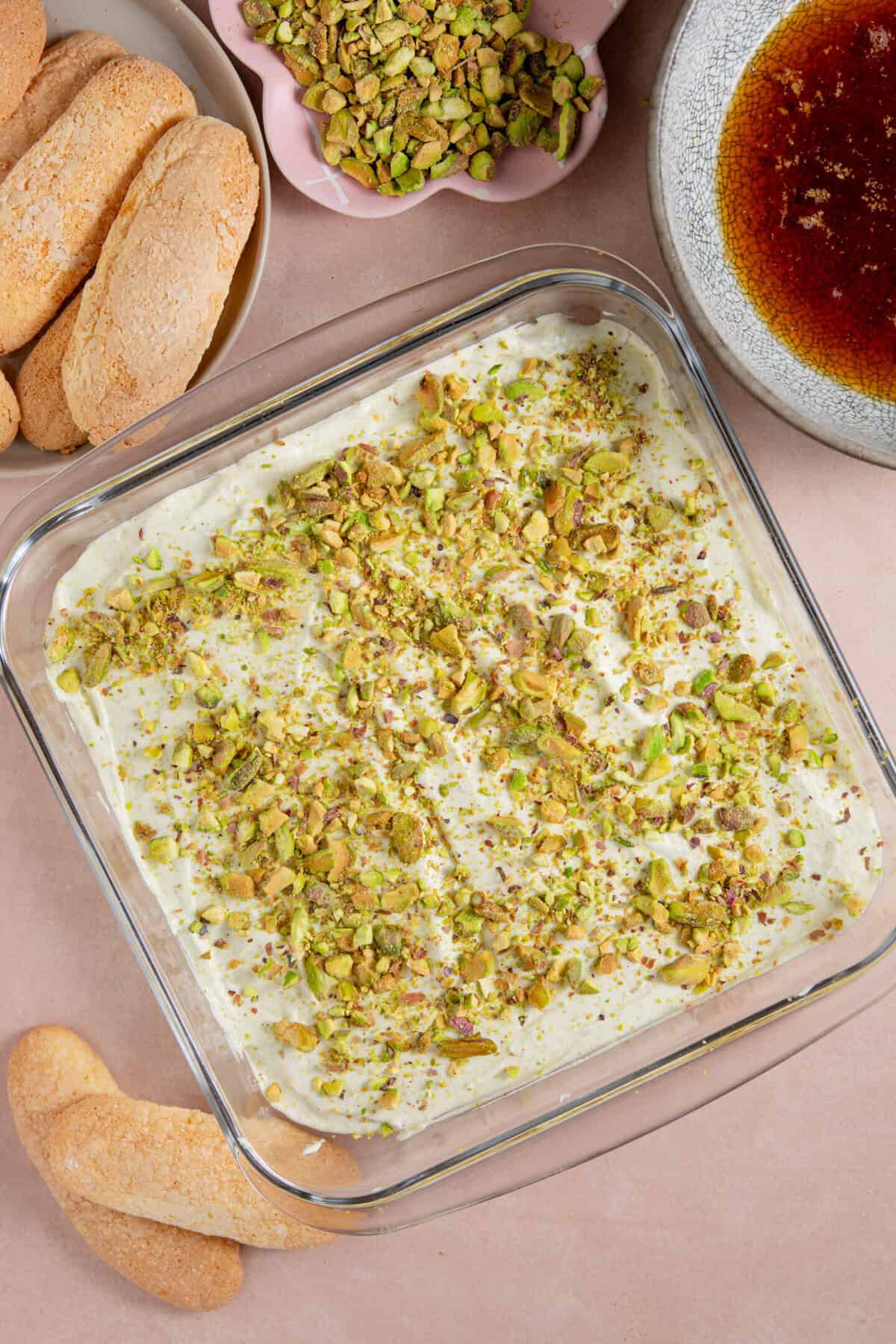 Layer the soaked sponge fingers, then a layer of cream with pistachio nuts on top.