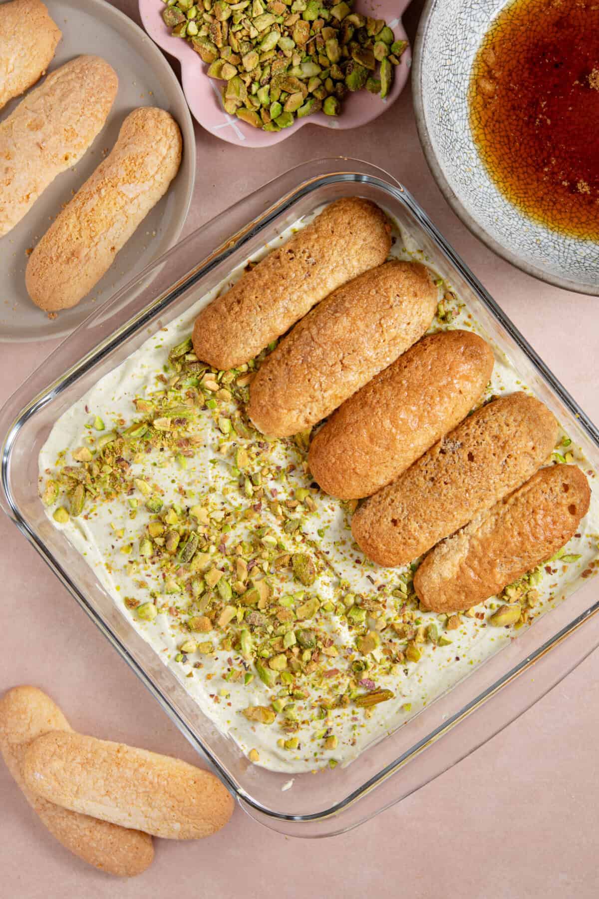 Process shot of a pistachio tiramisu showing the sponge fingers layered on top of the cream.