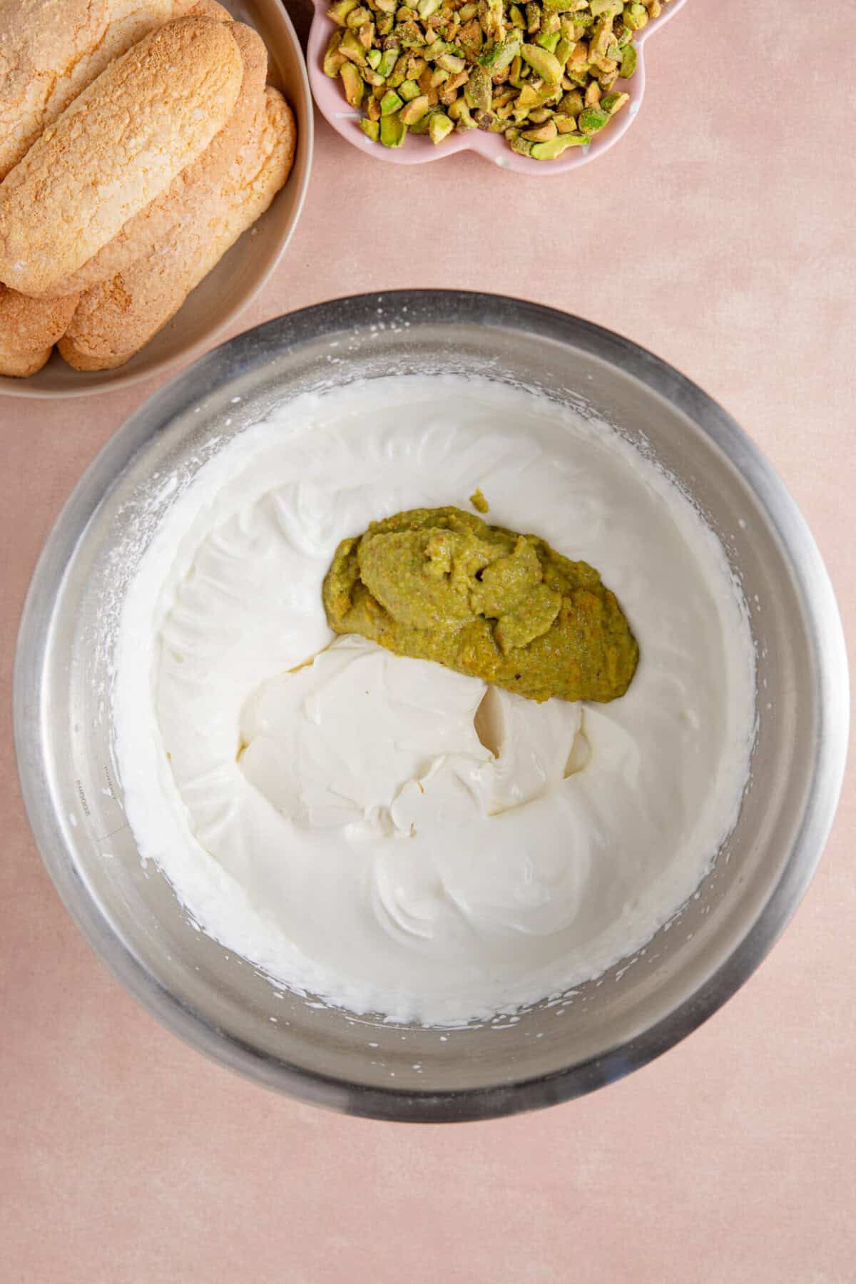 Process shot of a pistachio tiramisu recipe showing the mascarpone and pistachio cream added to the mixture.