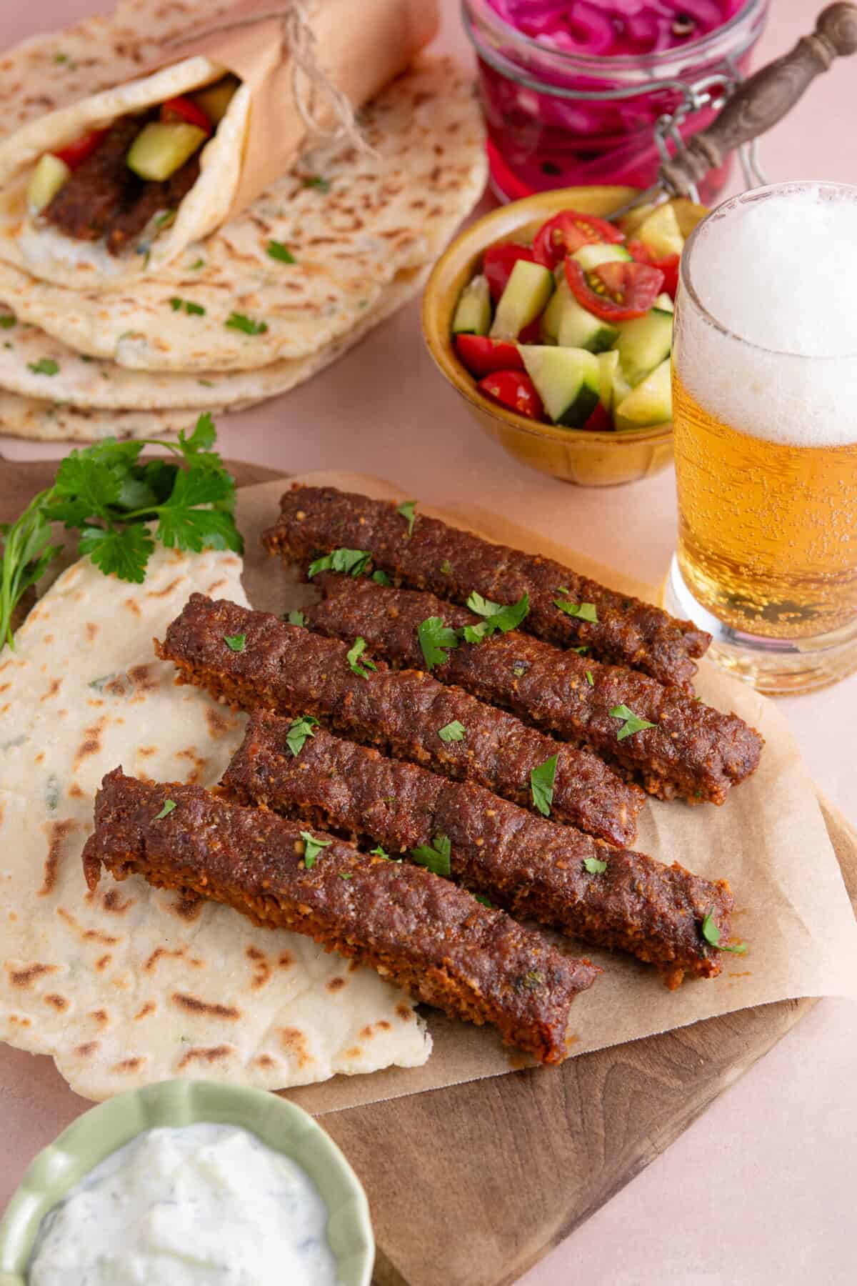 Strips of gluten free sheet pan beef kebabs on a flatbread with beer and salad in the background.