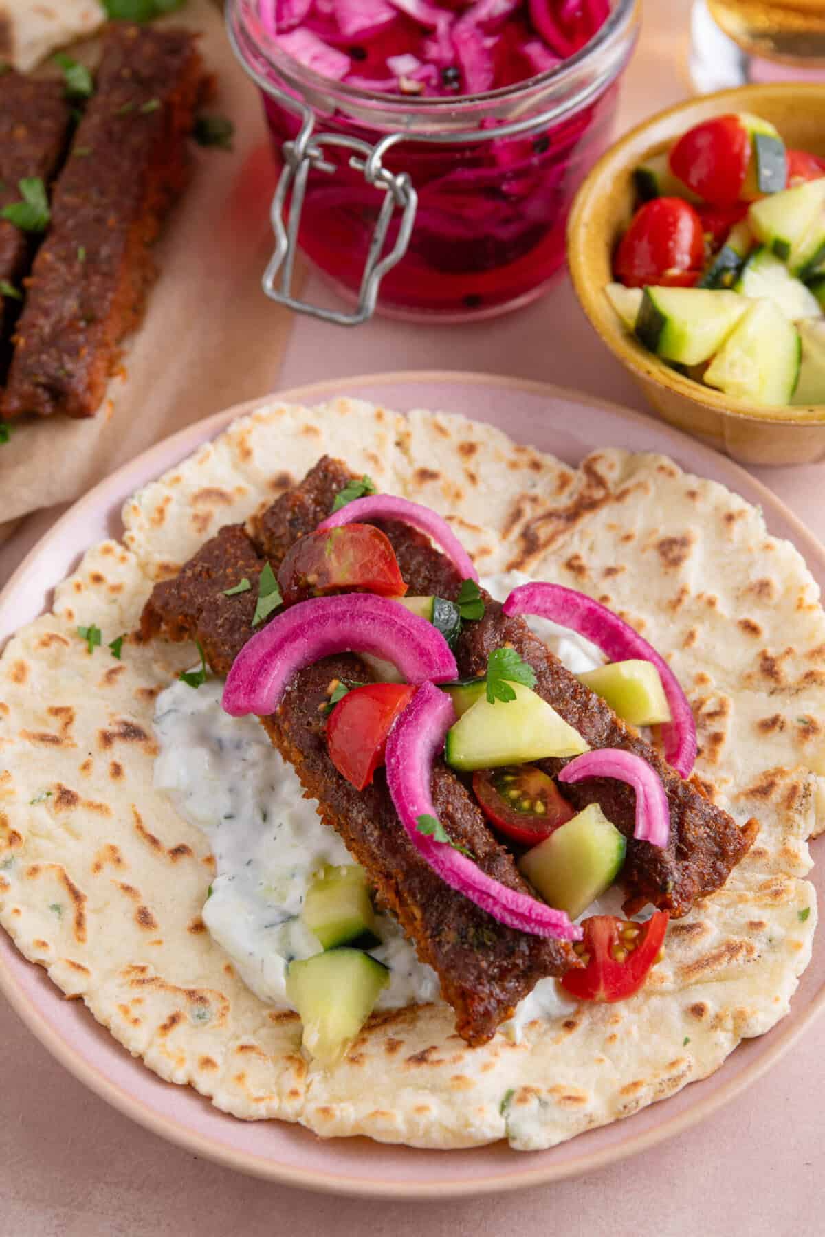 Process shot for sheet pan kebabs recipe showing the strips of beef kebab on a flatbread loaded with salad.