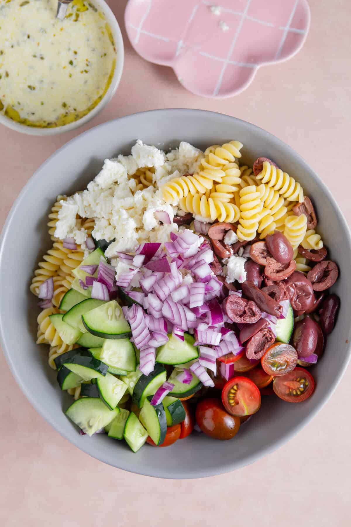 Process shot of a Greek pasta salad recipe showing all the pasta salad ingredients in a bowl before mixing.