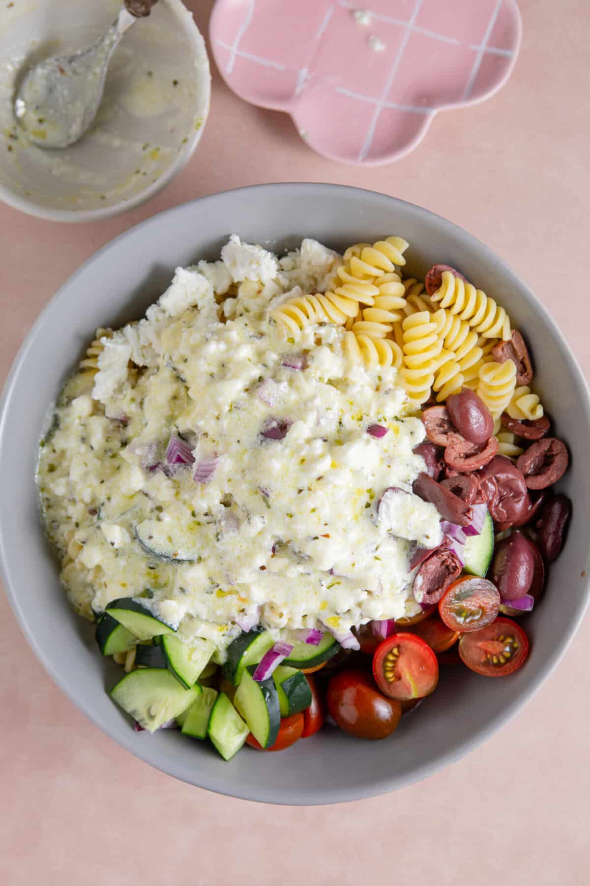 Process shot of a Greek pasta salad recipe showing the dressing poured over the pasta salad ready to mix.