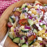 Close up of a bowl of Greek Pasta salad with red onions, olives, feta, tomato and cucumber.
