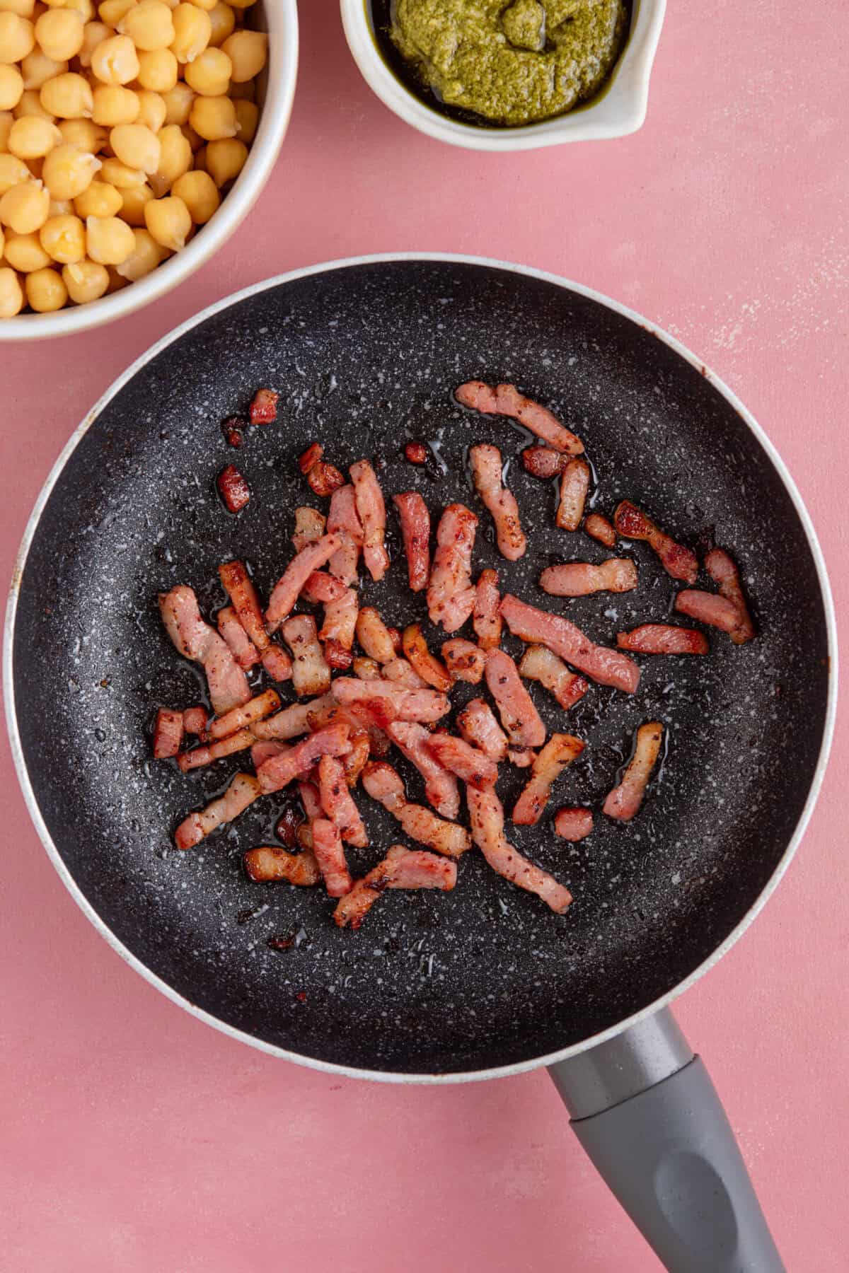 Process shot of gluten free pesto pasta salad recipe showing the bacon lardons frying in a pan.