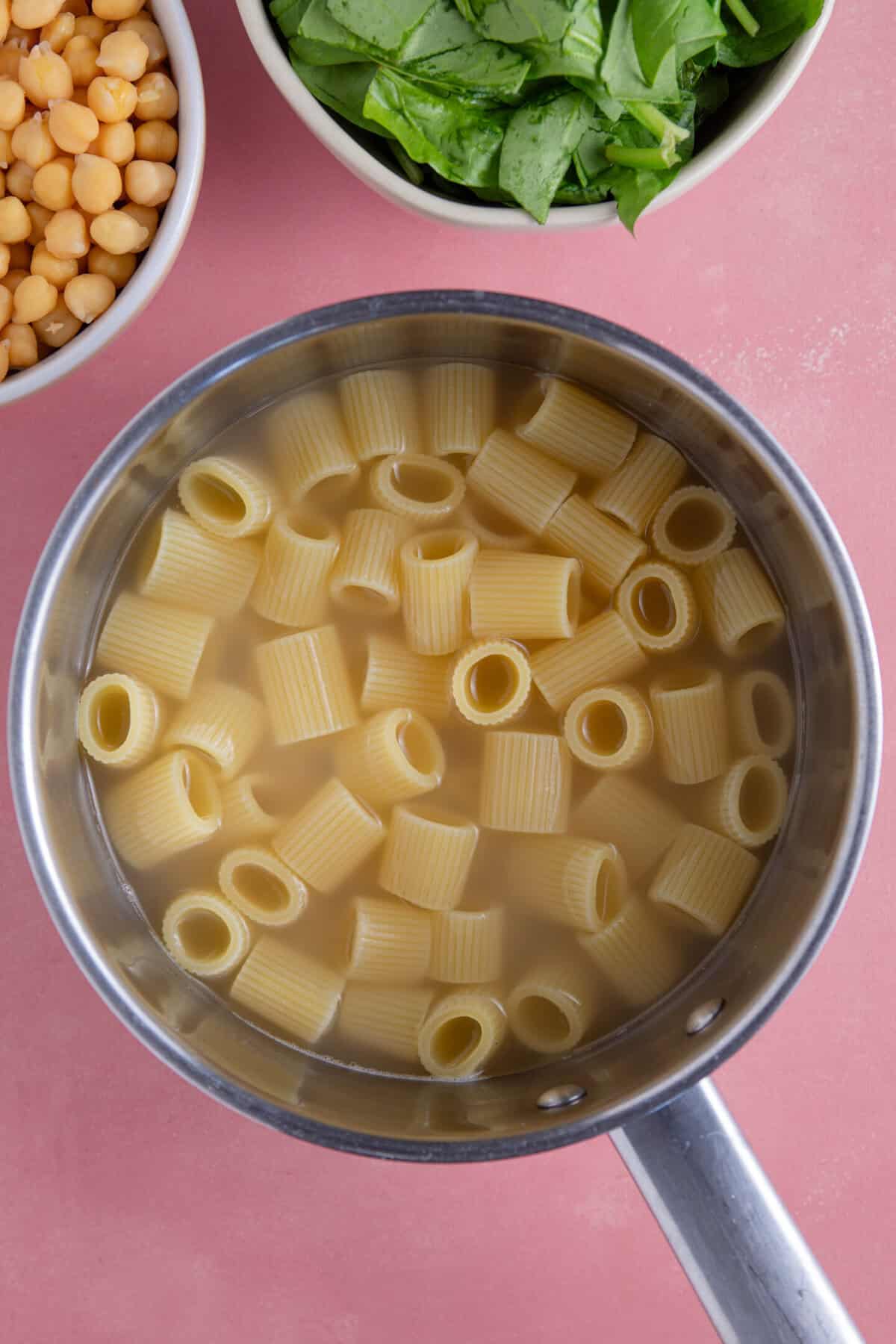 Process shot of gluten free pesto pasta salad recipe showing the pasta cooking in a pan.