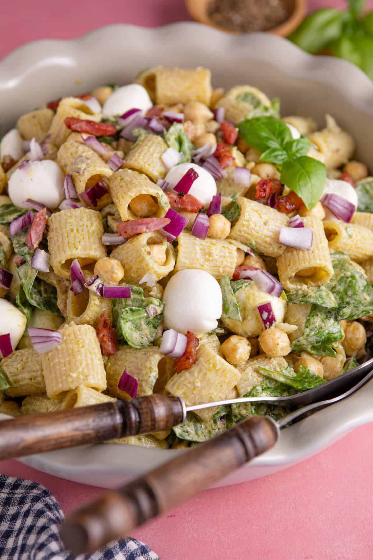 Close up of a gluten free pesto pasta salad with bacon, spinach and red onion.