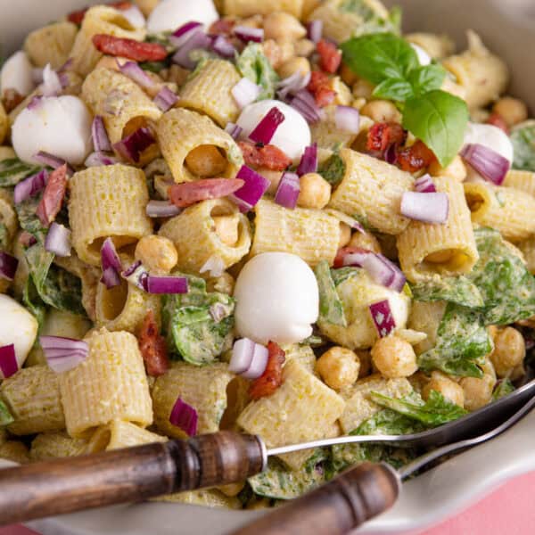 Close up of a gluten free pesto pasta salad with bacon, spinach and red onion.