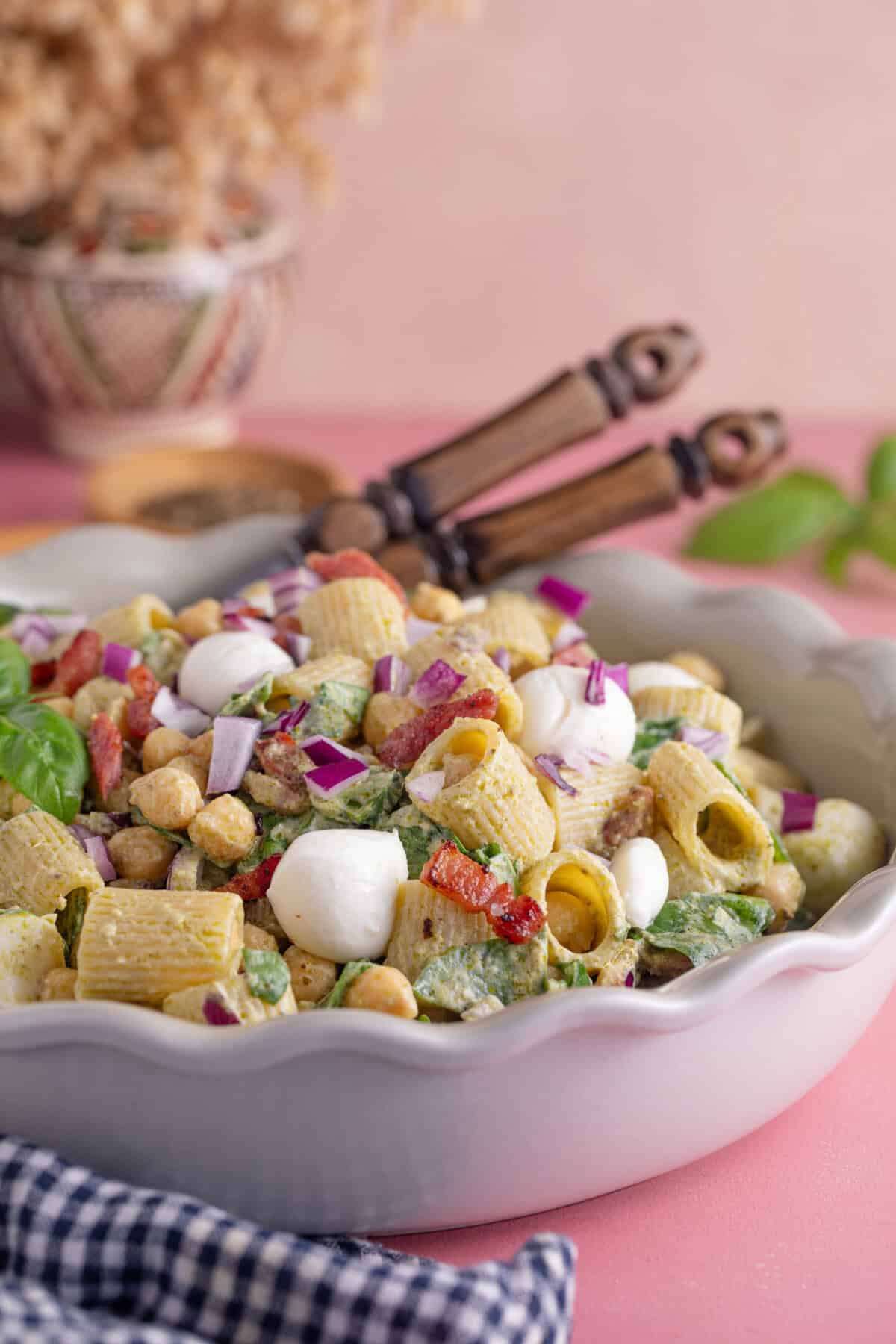 A bowl of gluten free pesto pasta salad with serving spoons.