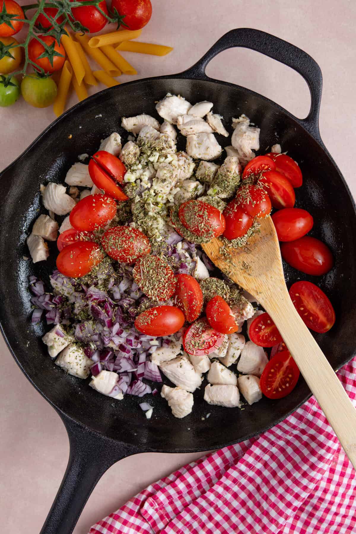 Process shot of creamy chicken tomato recipe showing chicken, tomatoes, red onion and herbs in a pan.