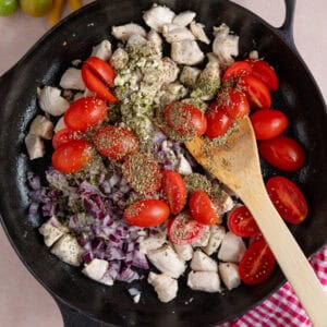Process shot of creamy chicken tomato recipe showing chicken, tomatoes, red onion and herbs in a pan.