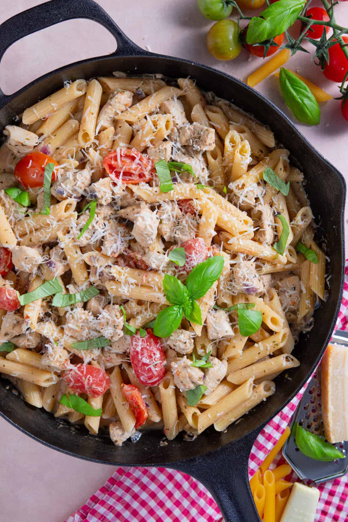 Close up of a pan of creamy chicken and tomato pasta with parmesan and basil on top.