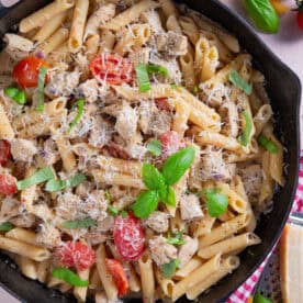 Close up of a pan of creamy chicken and tomato pasta with parmesan and basil on top.