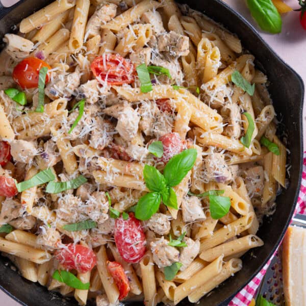 Close up of a pan of creamy chicken and tomato pasta with parmesan and basil on top.