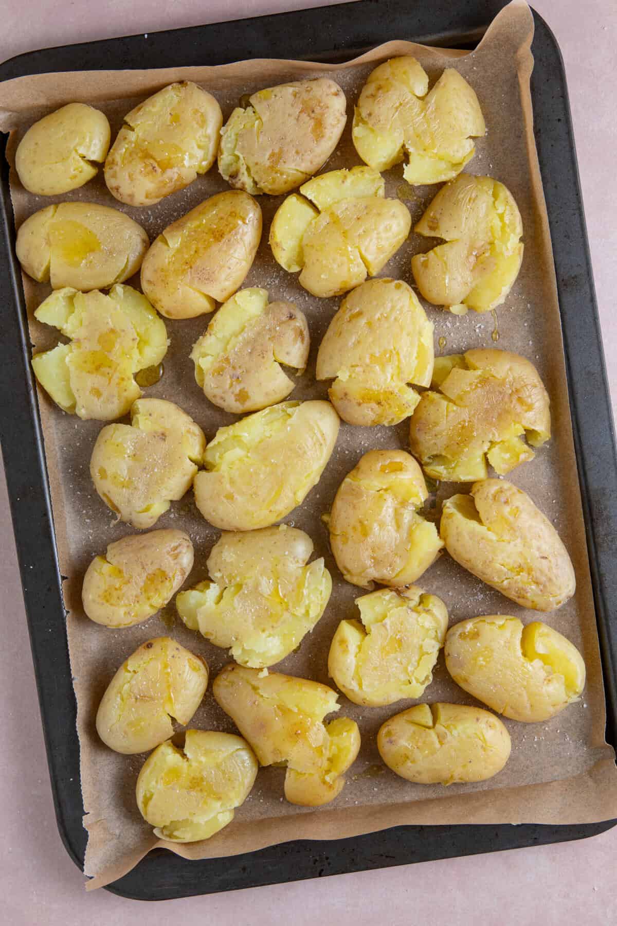 Process shot of chimichurri smashed potatoes recipe showing the cooked potatoes laid out 'smashed' on a baking tray.