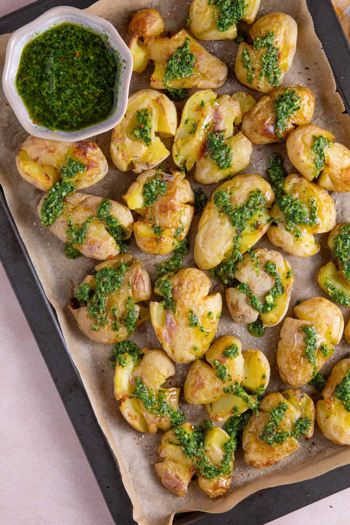 Process shot of chimichurri smashed potatoes recipe showing the finished smashed potatoes drizzled in the green sauce.