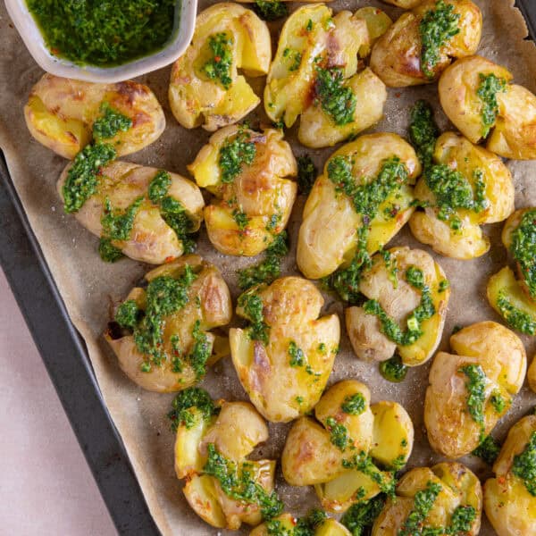 Process shot of chimichurri smashed potatoes recipe showing the finished smashed potatoes drizzled in the green sauce.