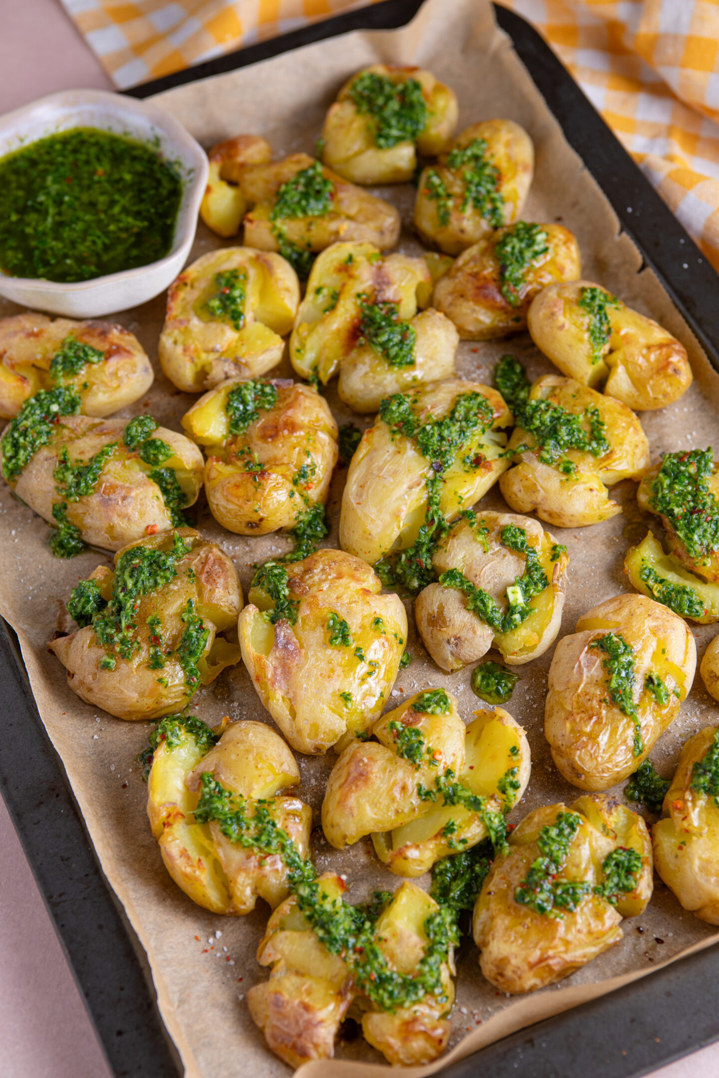 A tray of smashed potatoes drizzled with homemade chimichurri sauce.