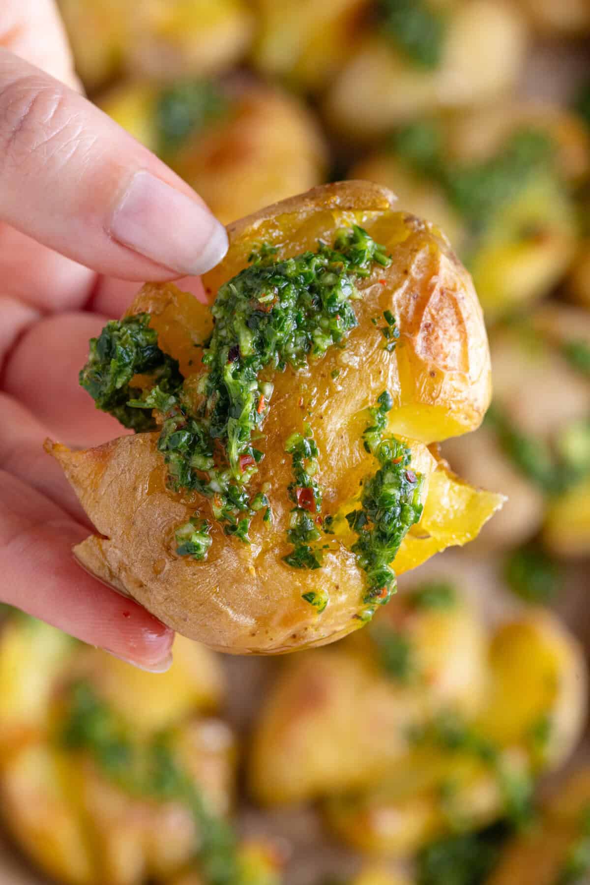 A hand holding a smashed potato covered in chimichurri sauce.