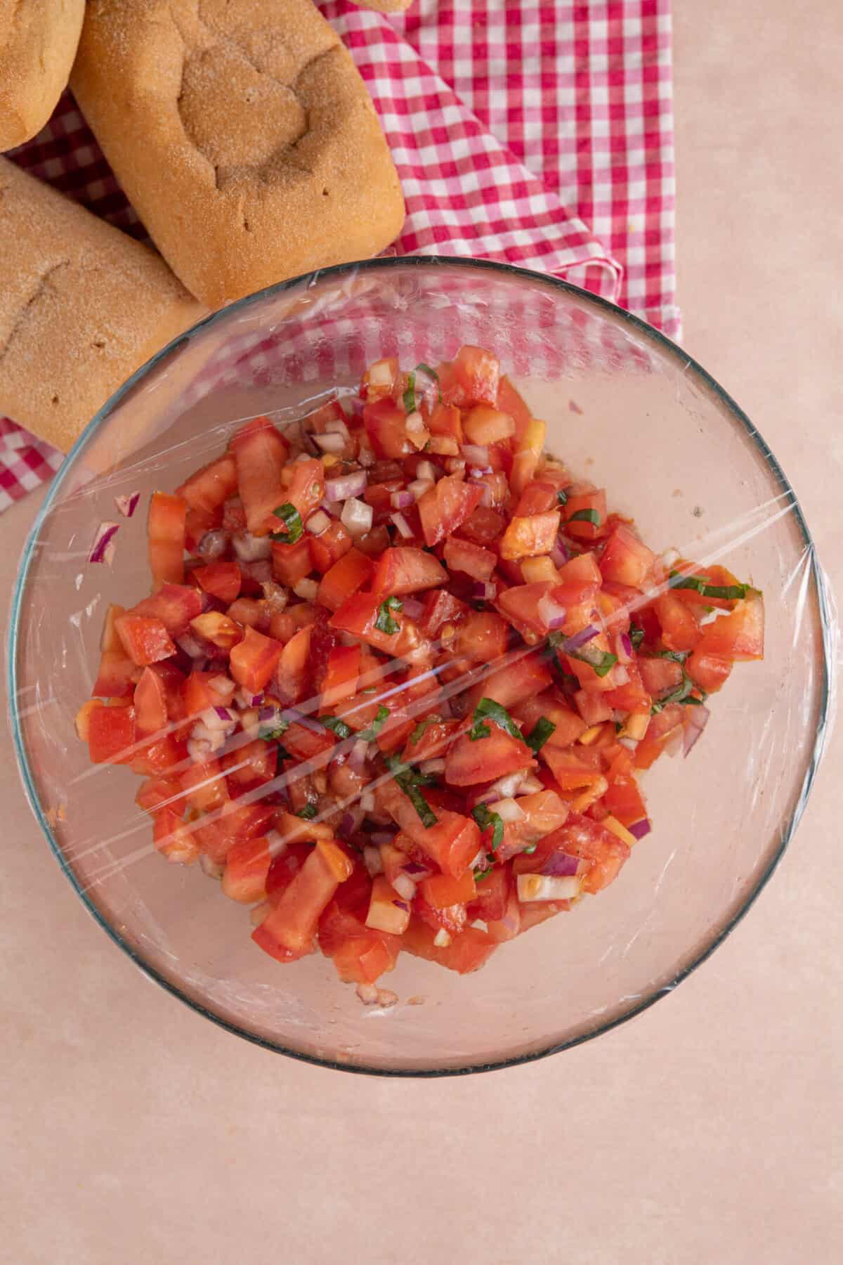 Process shot for gluten free bruschetta showing the tomato mixture in a bowl wrapped in clingfilm.