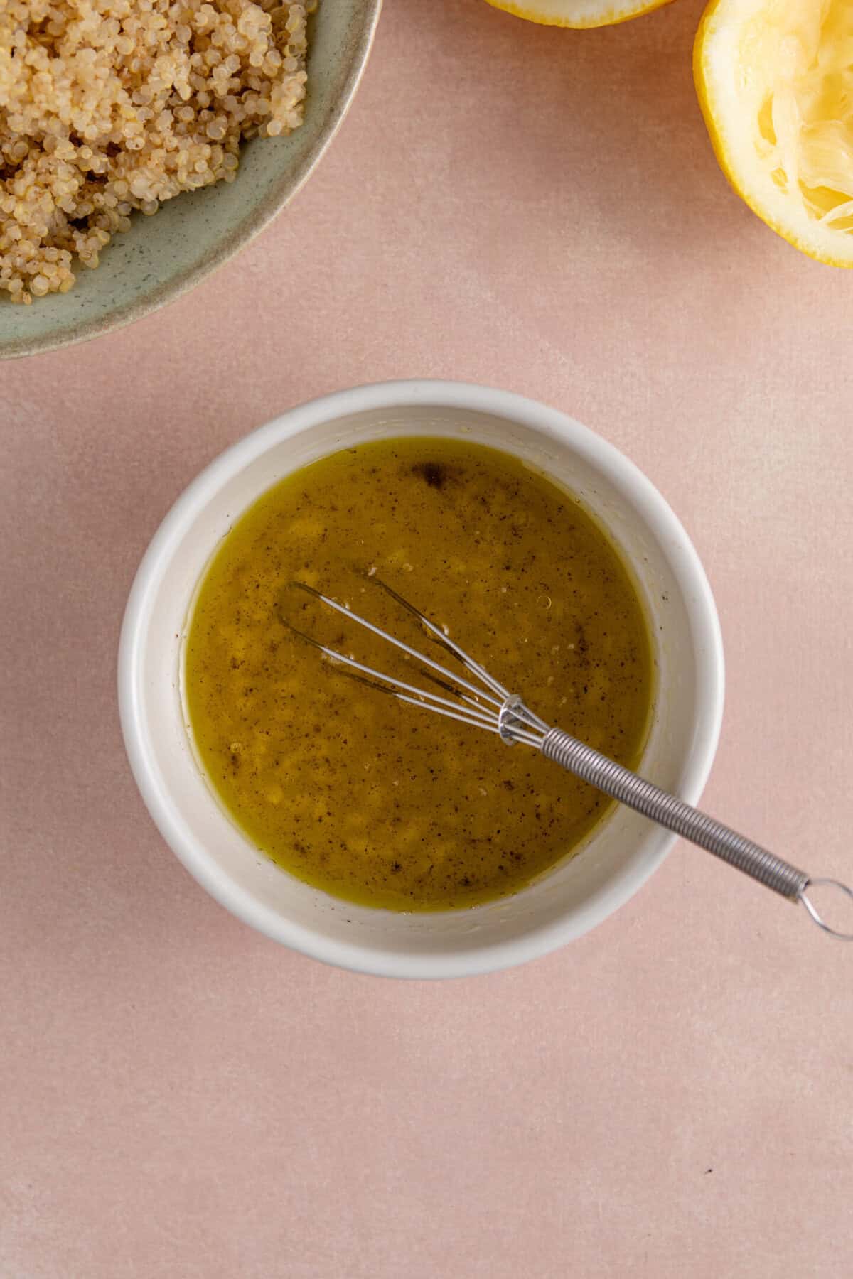 Process shot of gluten free tabbouleh recipe showing the lemon and olive oil dressing in a bowl with a small whisk.