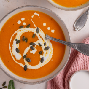 A bowl of pumpkin soup topped with pumpkin seeds and a swirl of cream.