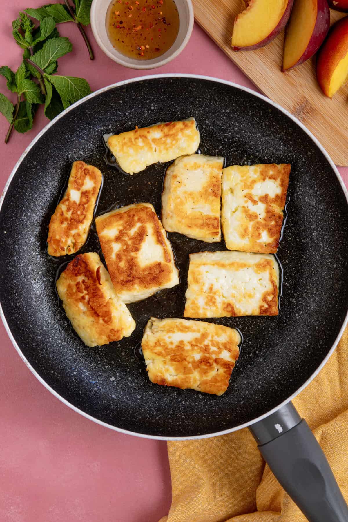 Process shot of peach and halloumi salad recipe showing the halloumi slices frying in a pan.