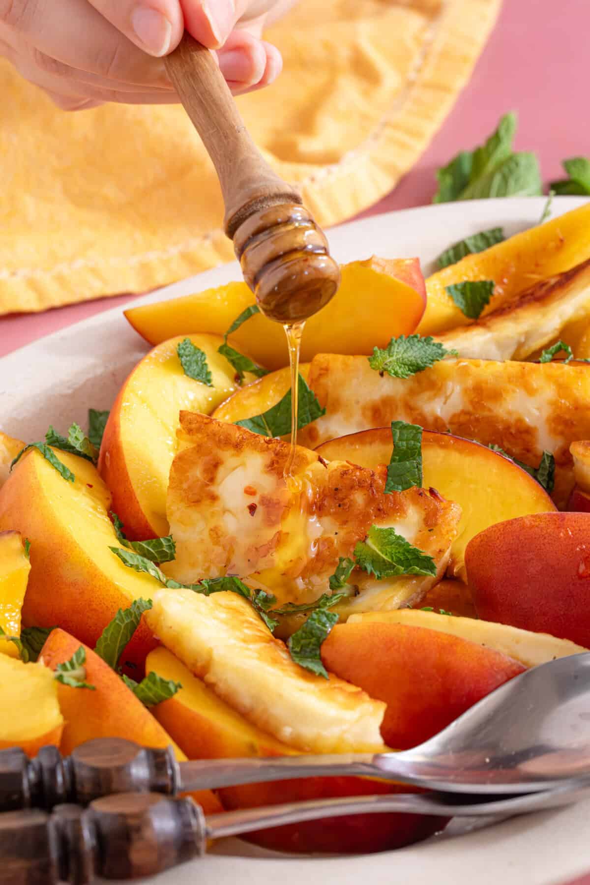 Hot honey being drizzled over slices of peach and grilled halloumi.