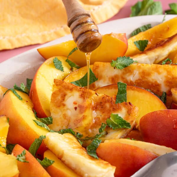 Hot honey being drizzled over slices of peach and grilled halloumi.