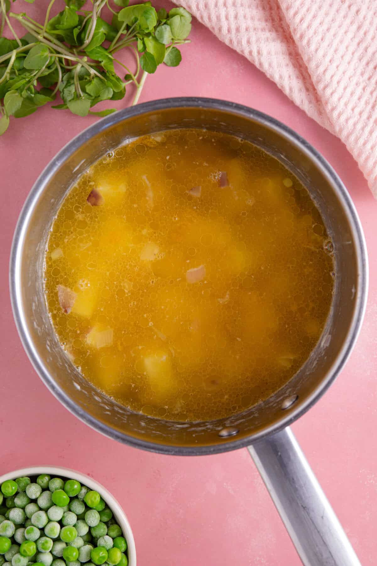 Process shot for watercress soup recipe showing the potatoes and shallots cooking in the stock.