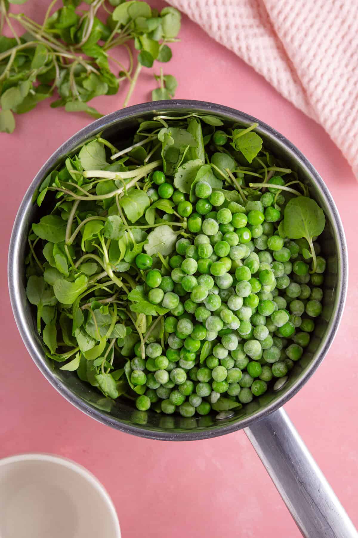 Process shot for watercress soup recipe showing the peas and watercress added to a saucepan.