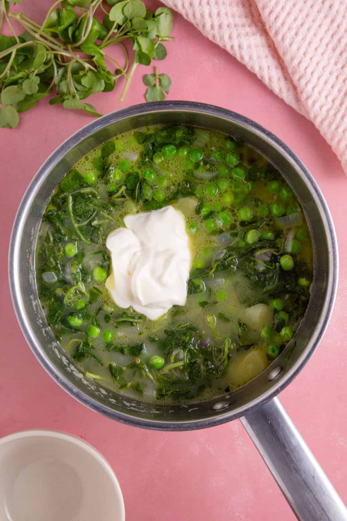 Process shot for watercress soup recipe showing the creme fraiche added to the pan of soup before it's blended.
