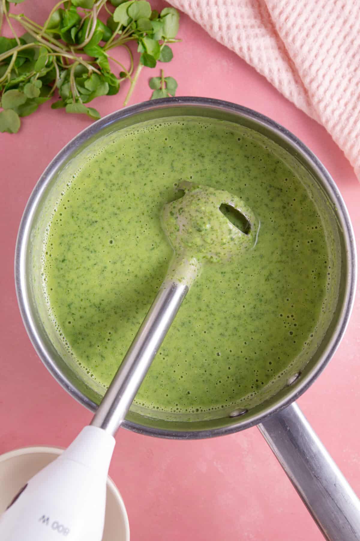 Process shot for watercress soup recipe showing the soup being blended using a stick blender.