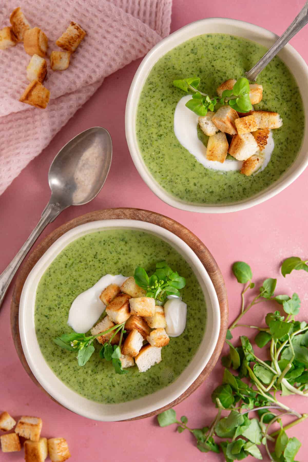 Process shot for watercress soup recipe showing two bowls of soup with a swirl of creme fraiche and croutons.