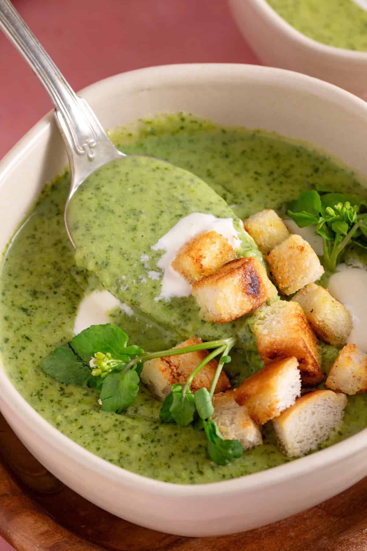 Close up of a spoonful of gluten free watercress soup topped with creme fraiche and gluten free croutons.