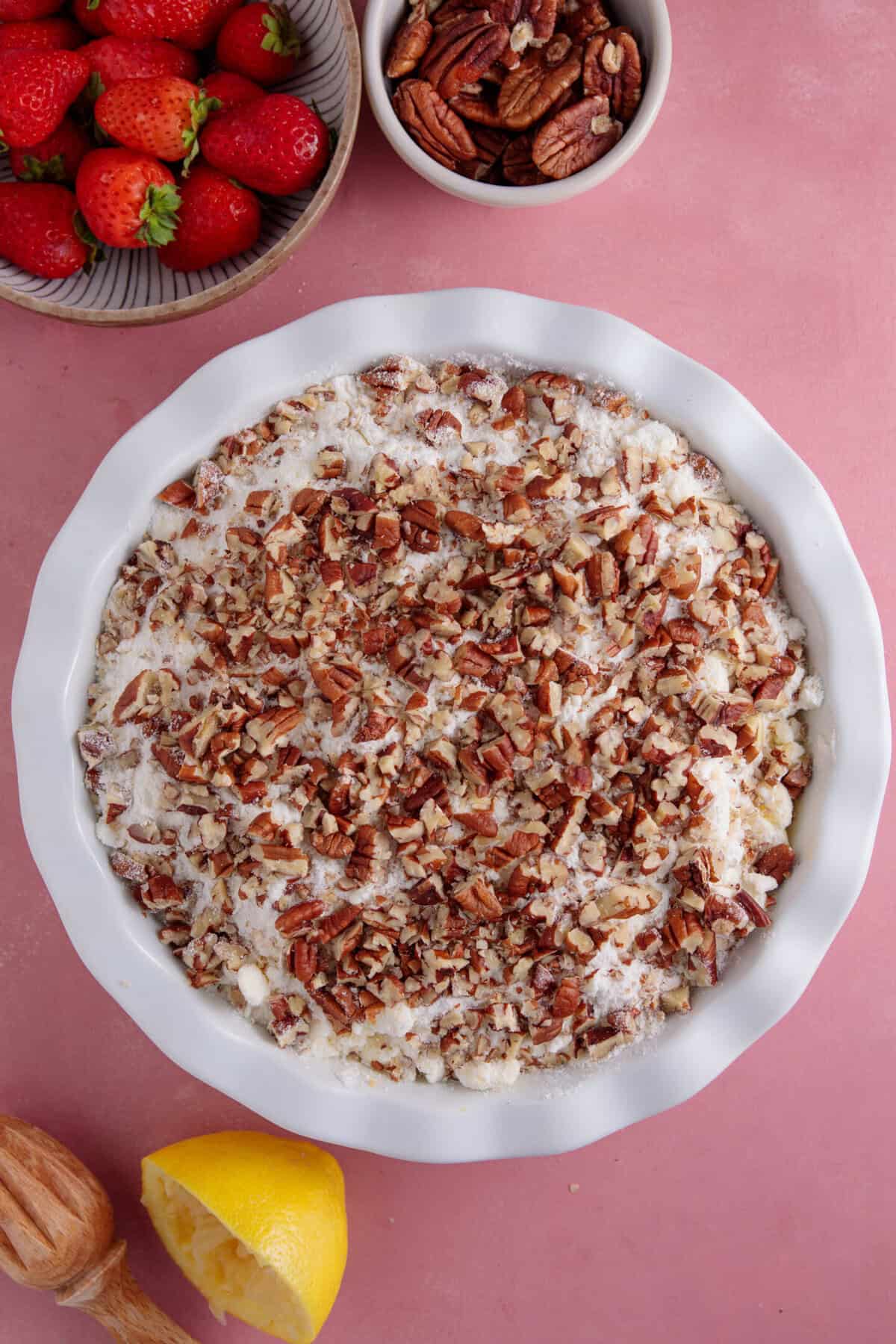 Process shot for apple and strawberry crumble recipe showing the unbaked crumble in a dish topped with pecans.
