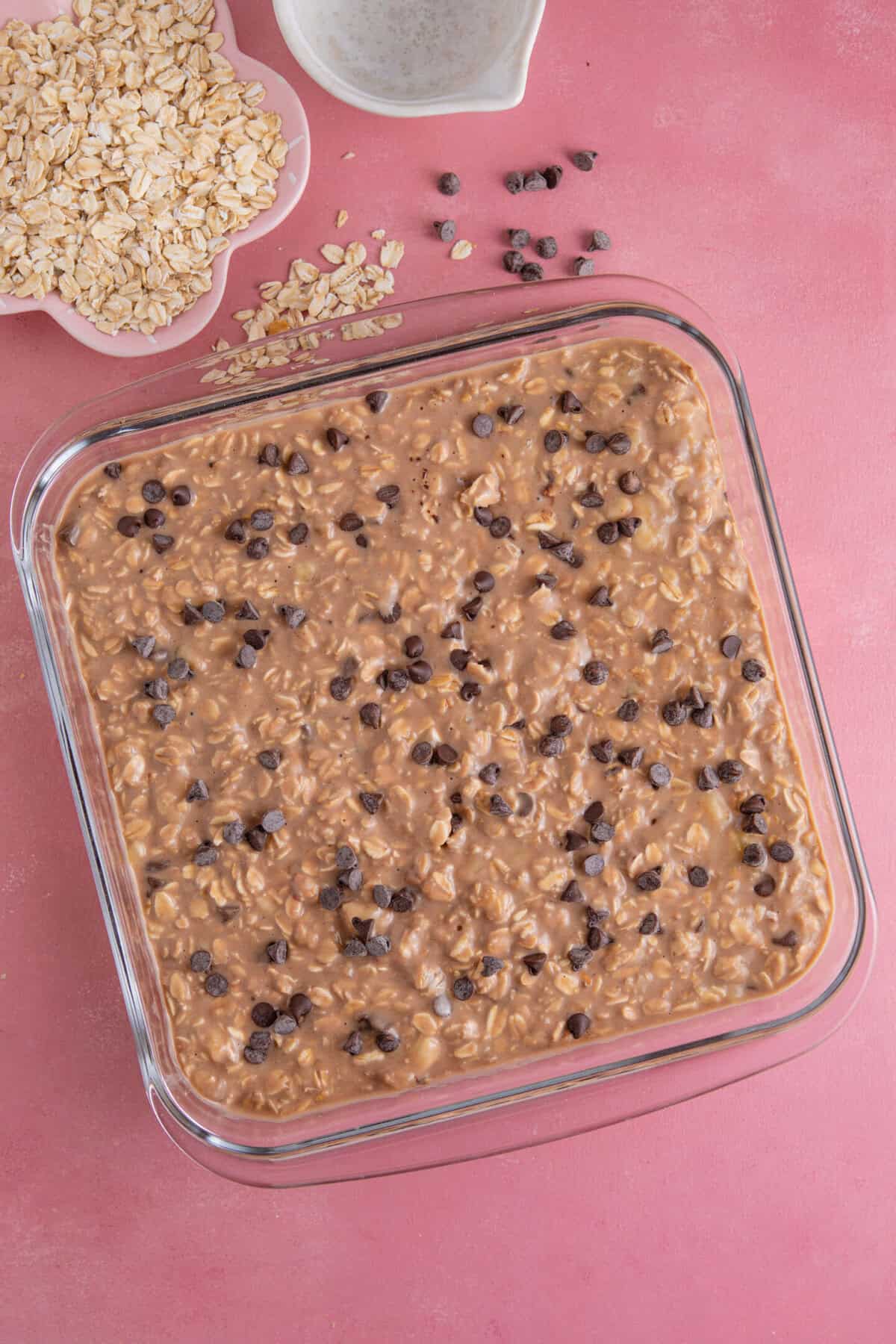 Process shot of banana baked oats showing the mixture in a glass baking dish, sprinkled with chocolate chips.