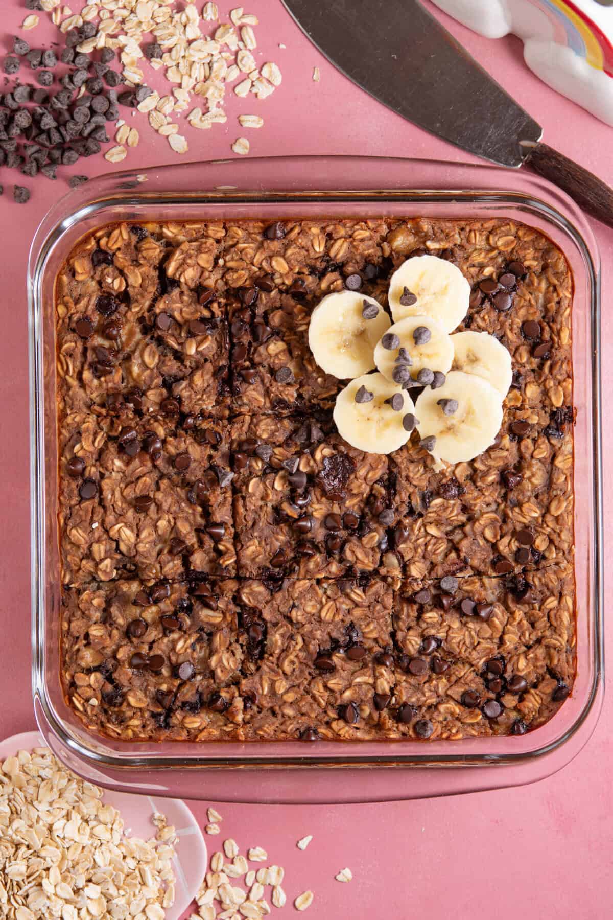 Process shot of banana baked oats showing the finished baked oats in a dish decorated with banana slices and choc chips.