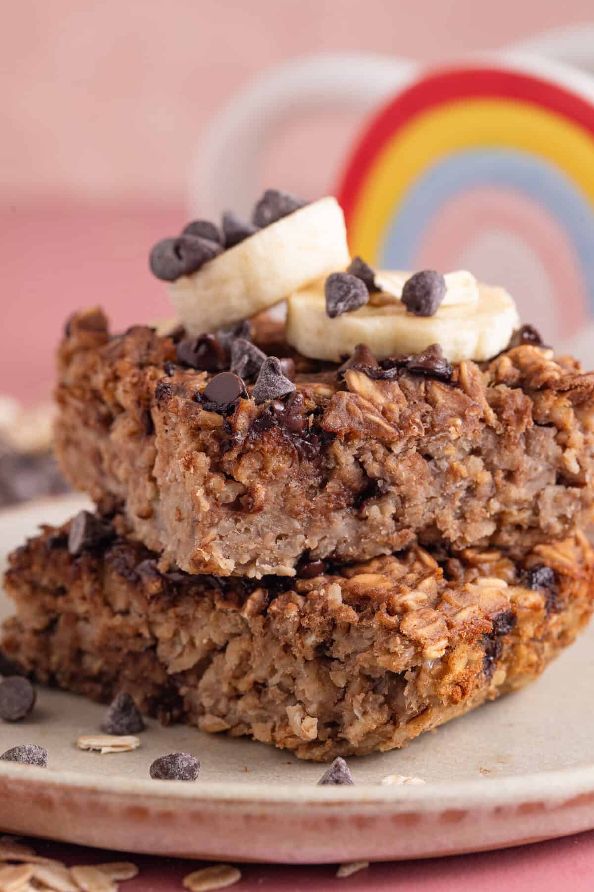 A stack of gluten free banana baked oat squares with slices of banana and choc chips on top.