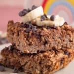 A stack of gluten free banana baked oat squares with slices of banana and choc chips on top.