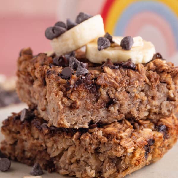A stack of gluten free banana baked oat squares with slices of banana and choc chips on top.