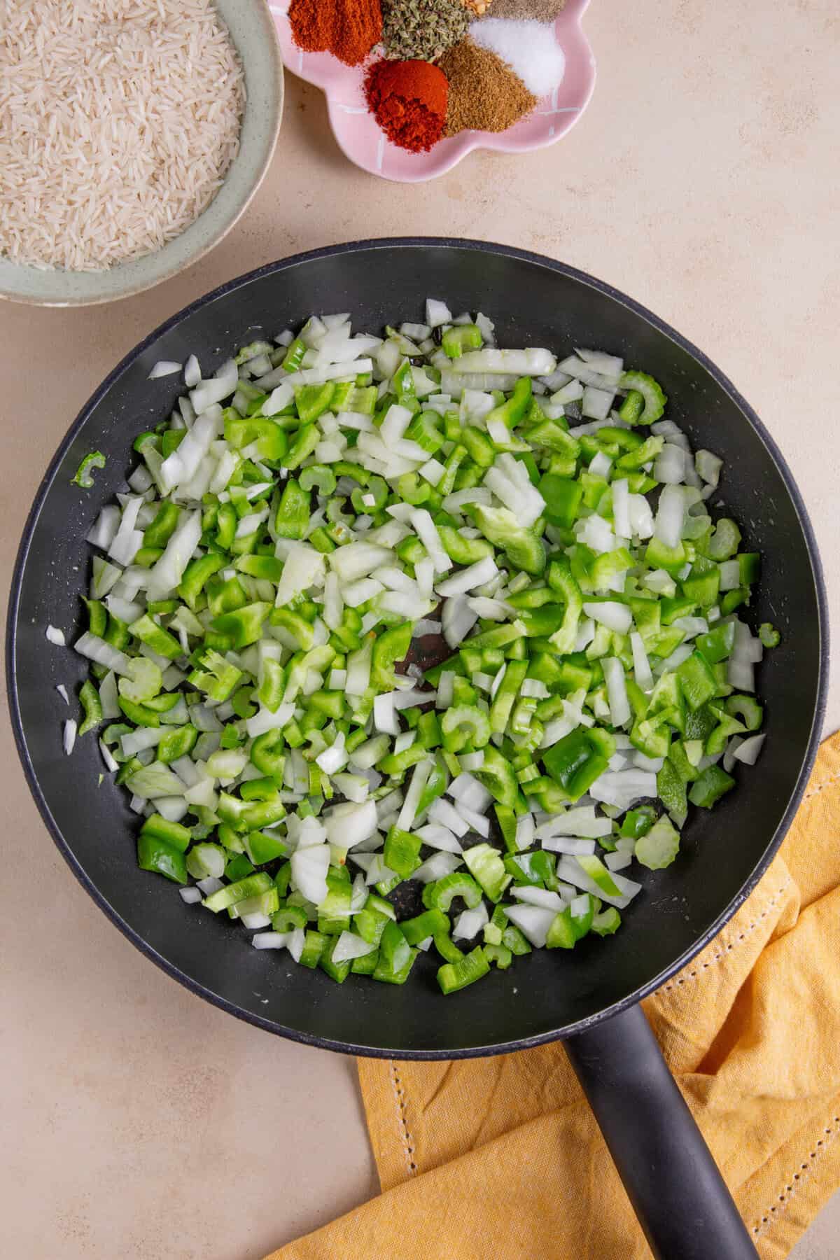 Process shot of cajun rice recipe showing the green peppers, celery and onion frying in a large pan.