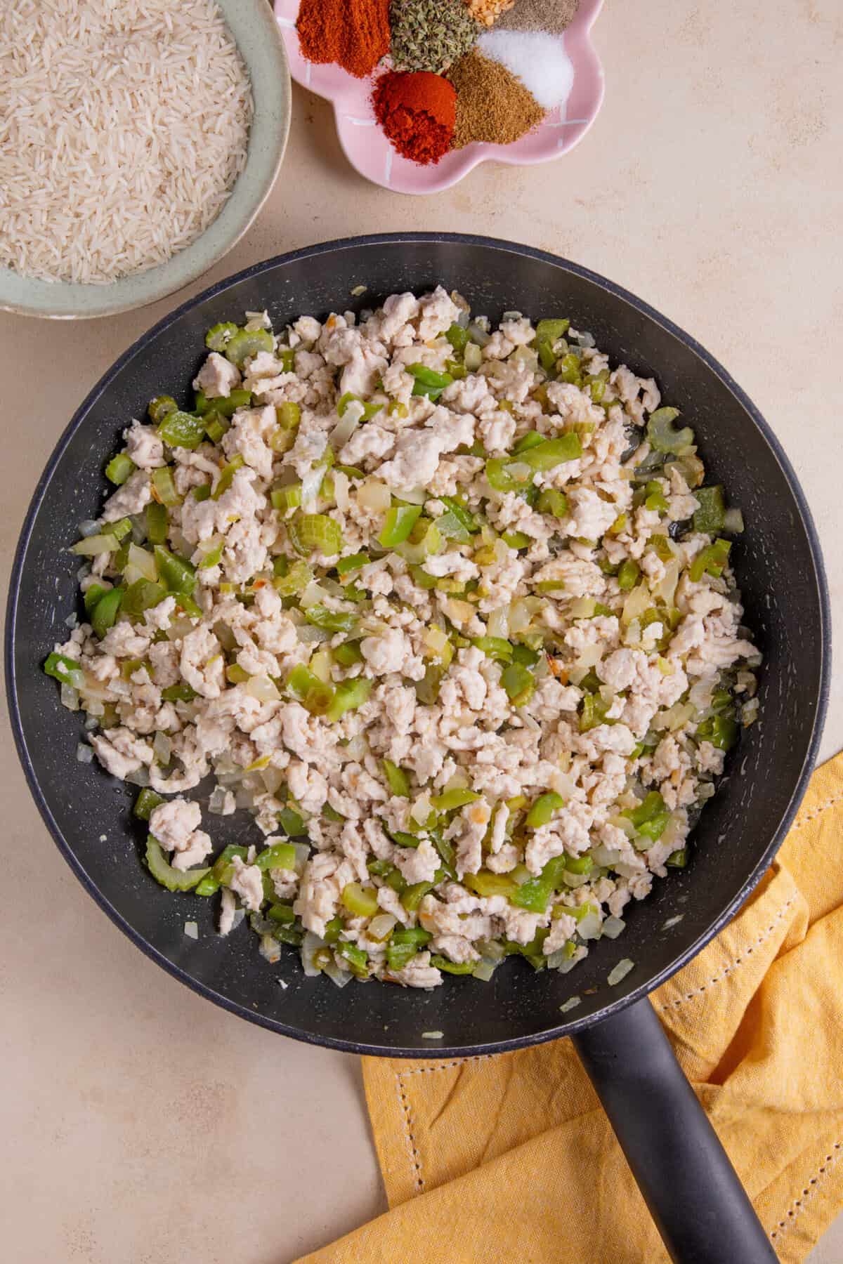 Process shot of cajun rice recipe showing onions, green pepper, celery and chicken mince in a frying pan.