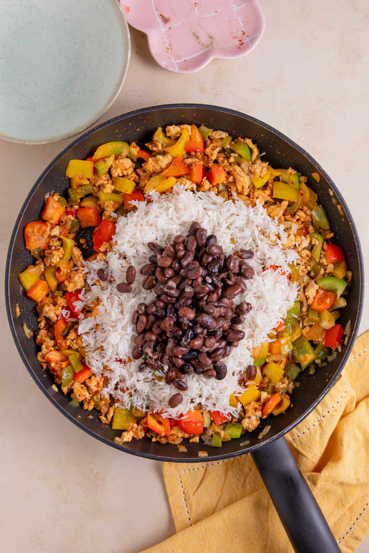 Process shot of cajun rice recipe showing the beans and rice added to a pan of peppers and chicken mince.