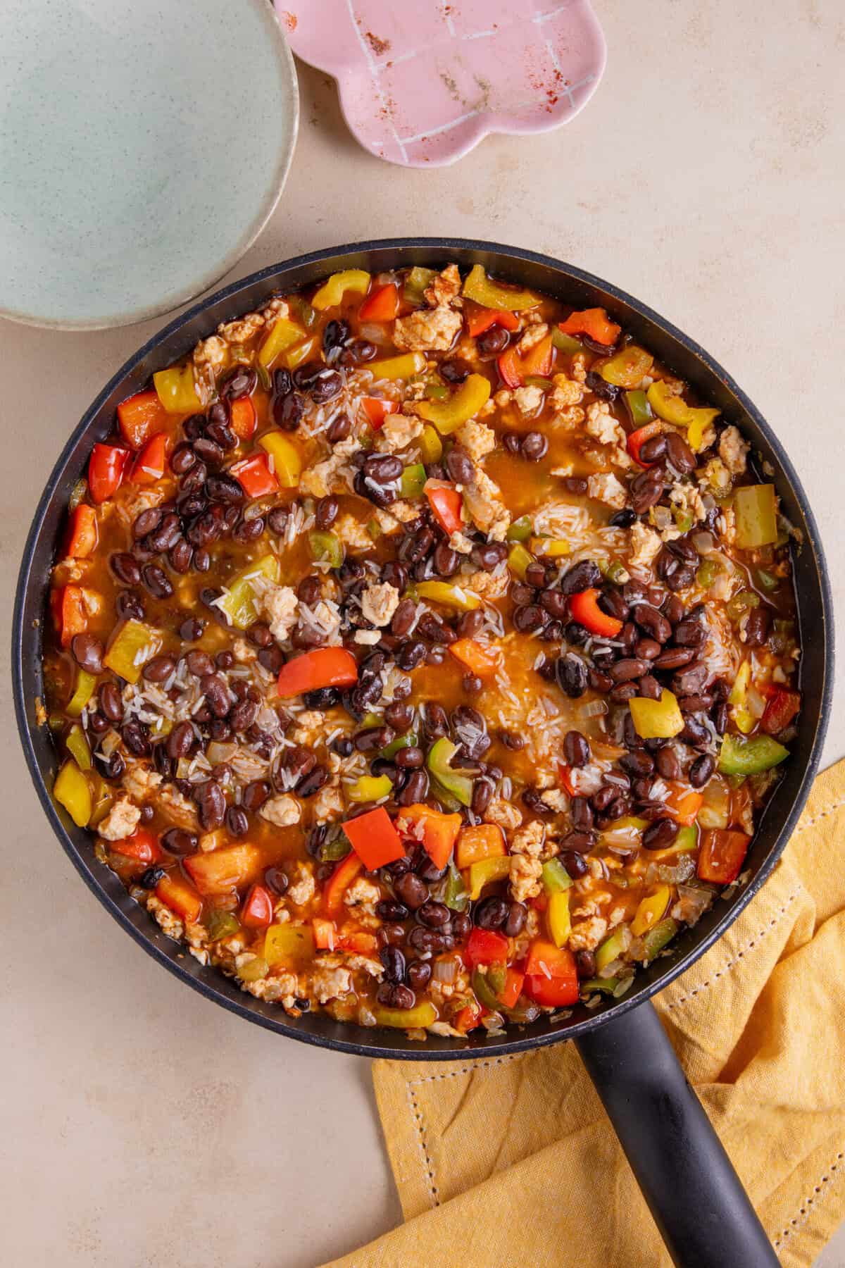 Process shot of cajun rice recipe showing the beans and rice added to a pan of peppers and chicken mince with chicken stock.