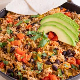 Close up of a pan of cajun rice topped with avocado and tortilla chips.