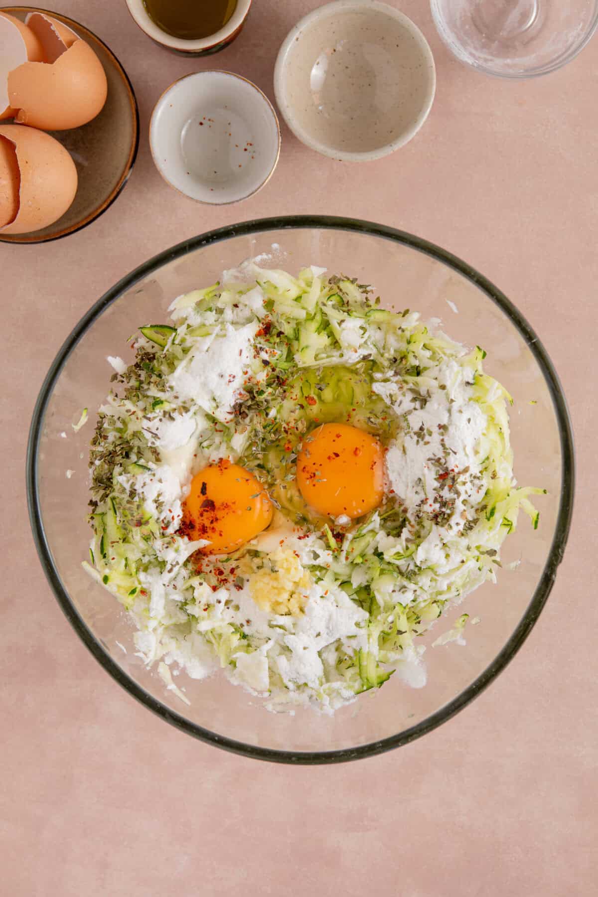 Process shot of courgette and halloumi fritters showing the eggs, flour, herbs, courgette and halloumi in a glass bowl.