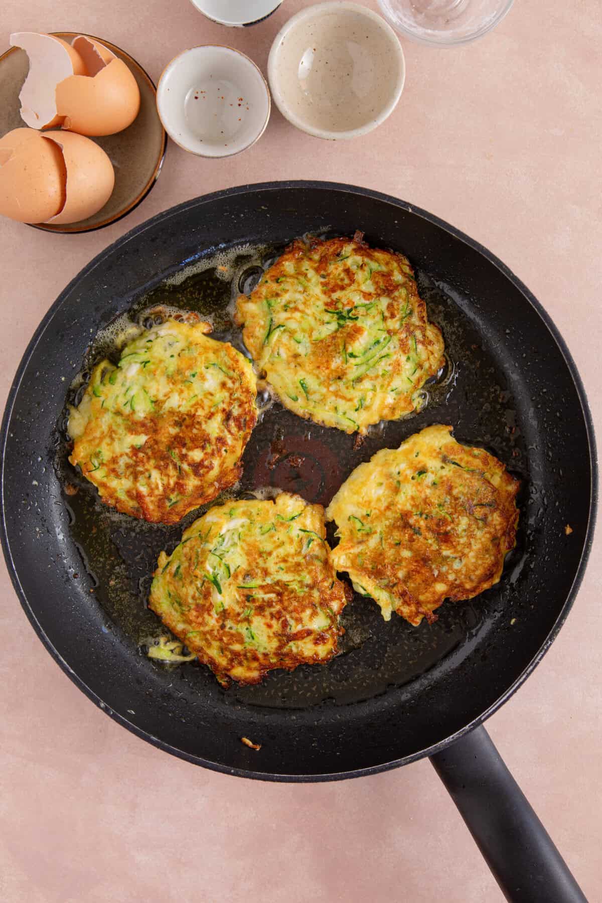 Process shot of courgette and halloumi fritters showing the cooked fritters in a pan.