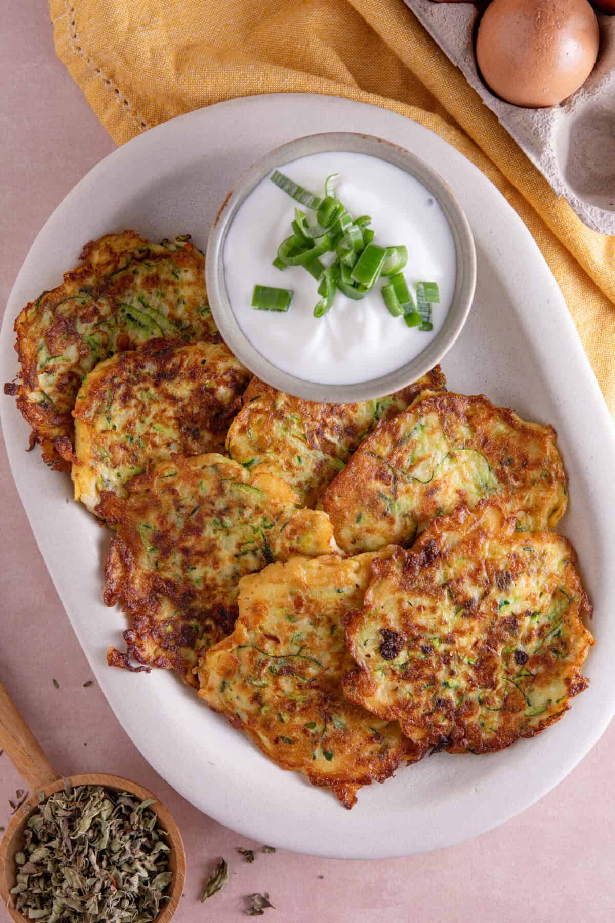 A plate of courgette and halloumi fritters with a garlic yoghurt dip on the side.