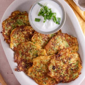 A plate of courgette and halloumi fritters with a garlic yoghurt dip on the side.